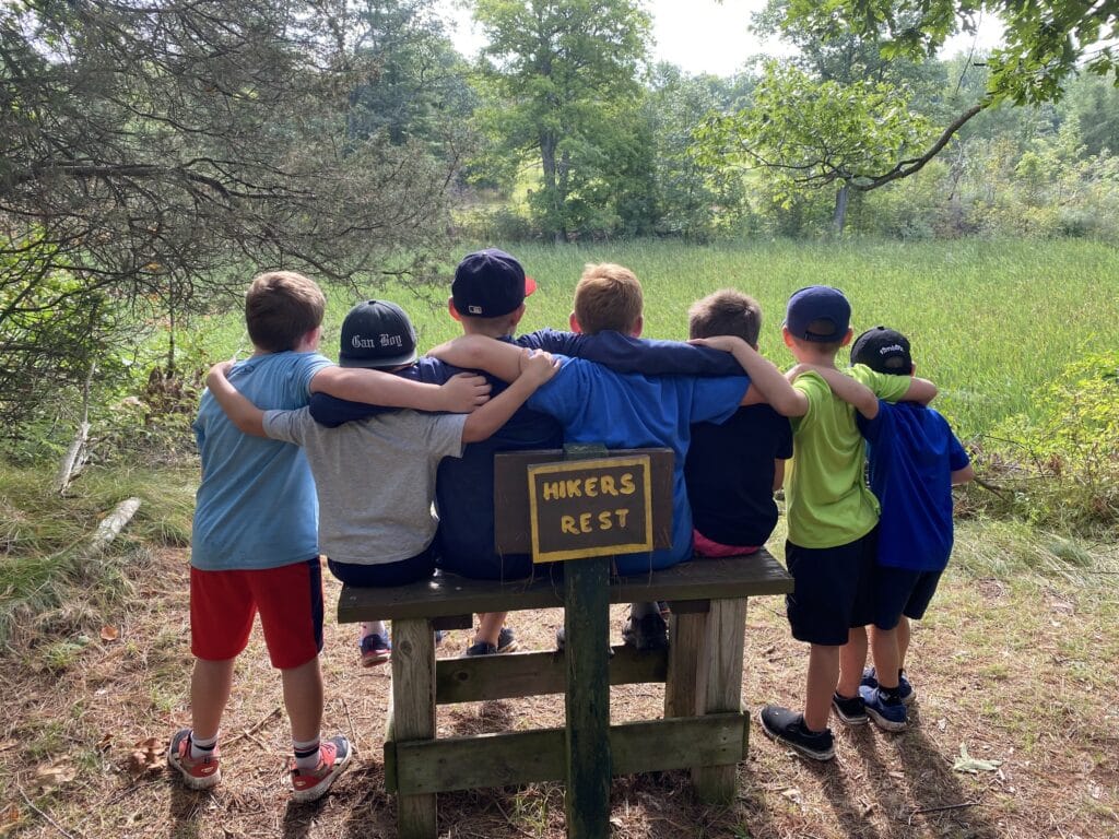 Group of kids in a park huddled together facing a pond