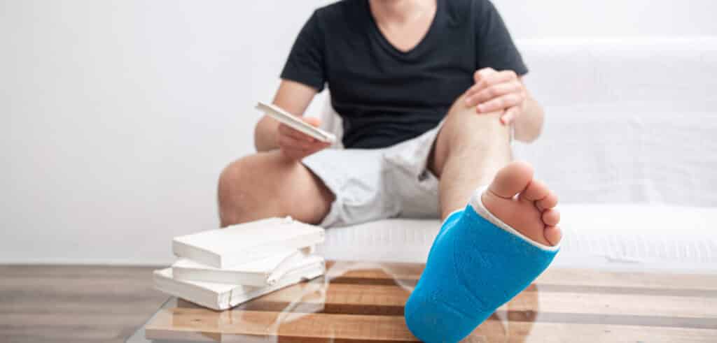 How to Prevent and Treat Blisters. Man with broken leg in blue splint for treatment of injuries from ankle sprain reading books at the home rehabilitation.