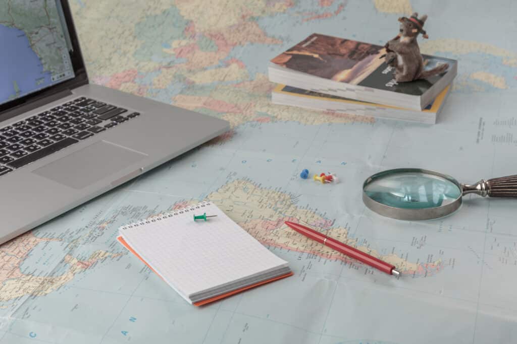 What Are The Benefits of Traveling? World map with a notebook, pen and magnifying glass.