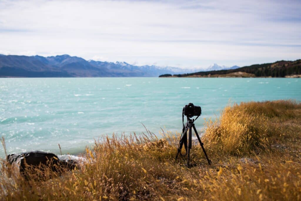 A view of a camera on a stand by the beautiful lake and the hills on the horizon on a sunny day. Getting started with nature photography blogs.