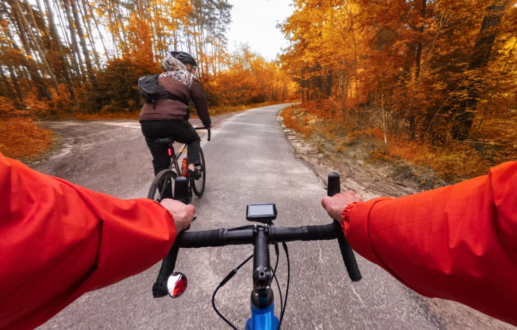 Outdoor Adventure Travel. Cyclists on bicycles ride along the road in the autumn forest. POV. Autumn cycling in the forest.