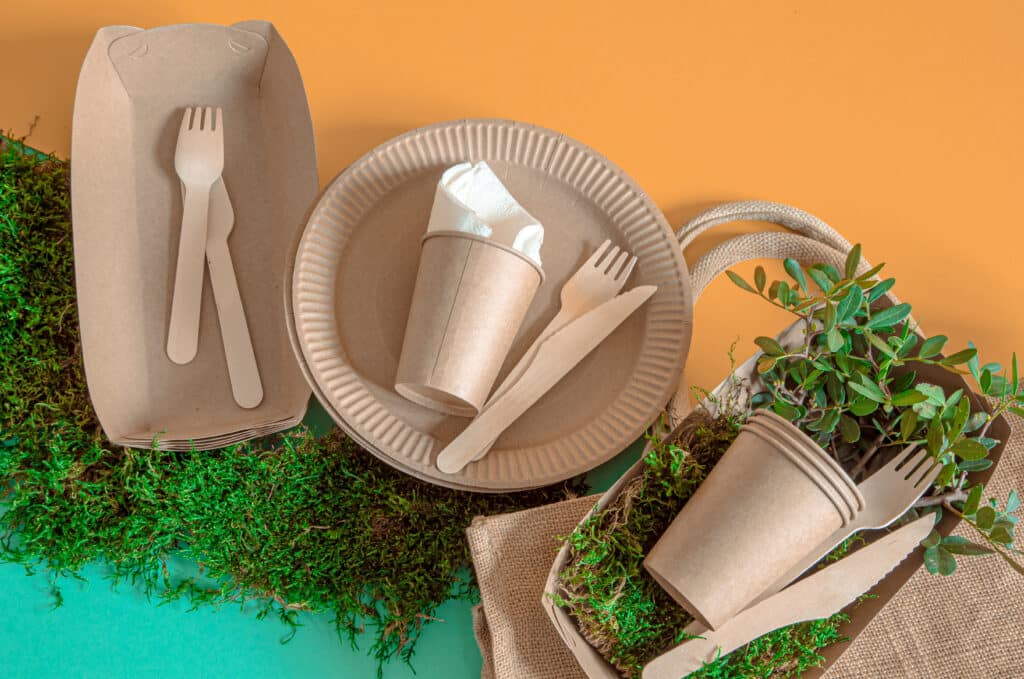Sustainable Food and Beverage. ECO craft paper tableware. Paper cups, plates, bag, fast food containers and wooden Cutlery with cornstarch on a colored orange-blue background. Recycling or the concept of zero waste. The view from the top.