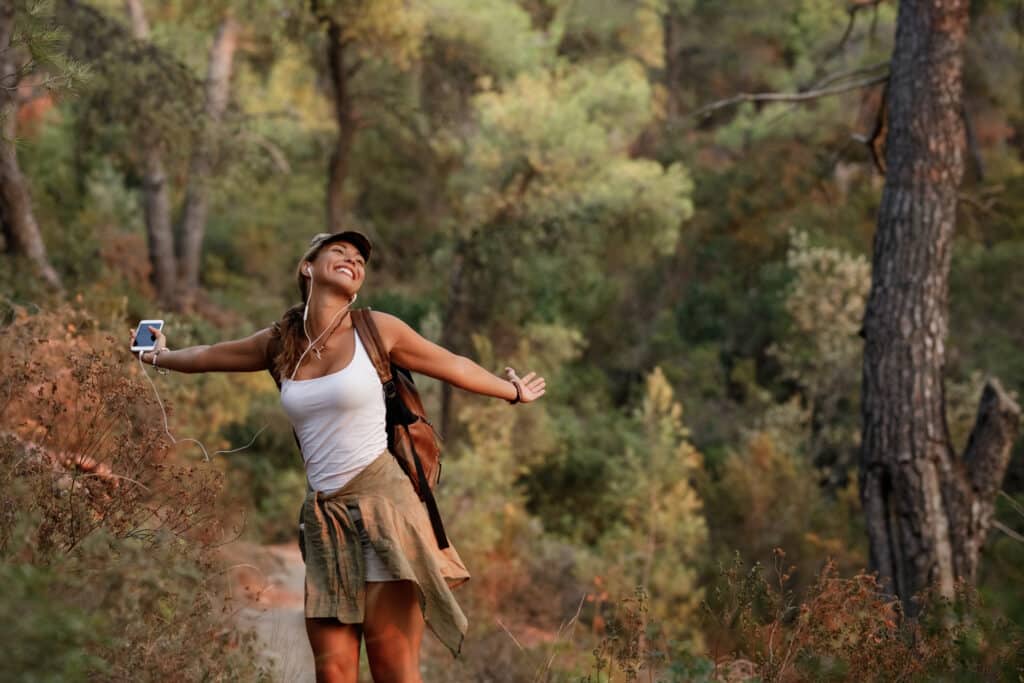 Outdoor Adventure Travel. Carefree woman hiking in nature and listening music over earphones.